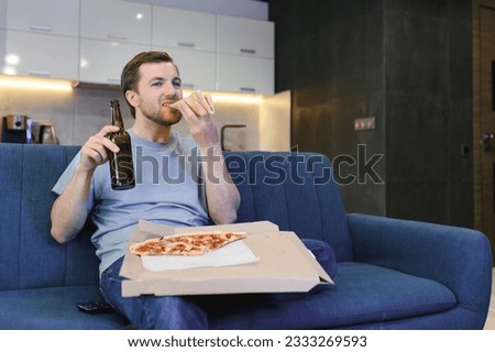 Happy young man drinking beer and eating pizza when watching game on tv at home.