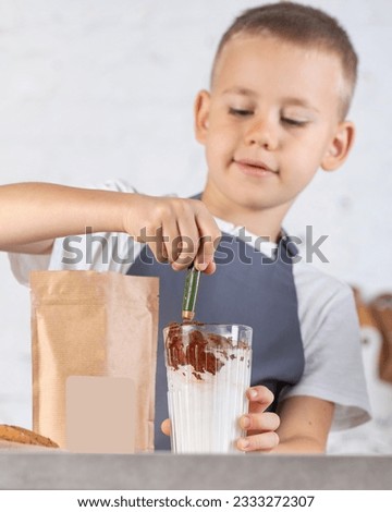 Cute boy cooks hot chocolate from cocoa powder and milk. A boy cooks cocoa in the kitchen.
