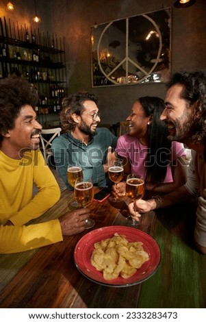 Vertical. Young people laughing and drinking in a pub. Group of friends celebrating a party together. A small gathering smiling in a club. millennials having fun in a bar indoors. Caucasian young guys Royalty-Free Stock Photo #2333283473