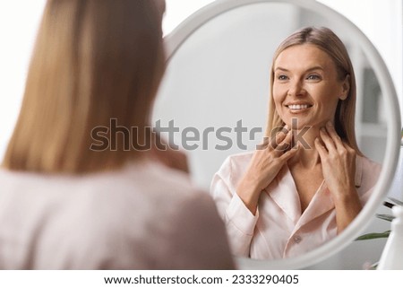 Beautiful Mature Woman Looking At Mirror And Touching Her Soft Skin On Neck, Attractive Middle Aged Female Smiling To Reflection, Enjoying Anti-Aging Skincare Routine At Home, Selective Focus Royalty-Free Stock Photo #2333290405