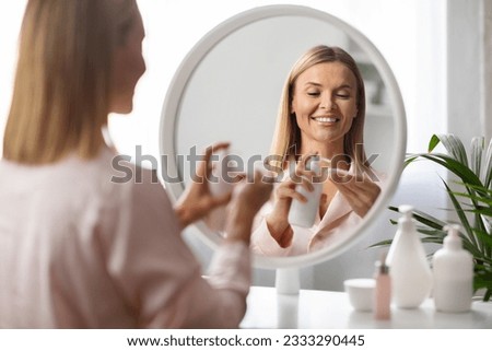 Beauty Routine. Smiling Middle Aged Woman Using Makeup Removal Milk And Cotton Pad For Skin Cleansing, Beautiful Mature Female Standing Near Mirror At Home, Enjoying Daily Skincare, Selective Focus Royalty-Free Stock Photo #2333290445