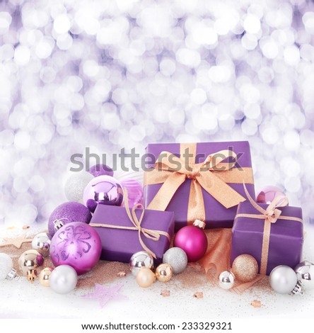 Colorful purple and gold Xmas gifts and baubles arranged in falling winter snow in square format with copyspace for your Christmas wishes or invitation to a seasonal party