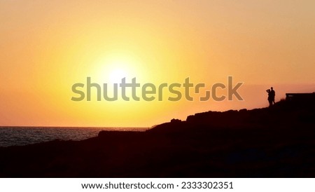 Romantic Sunset Silhouettes with Copyspace: Couple Gazing at the Sunset from Rocky Cliff