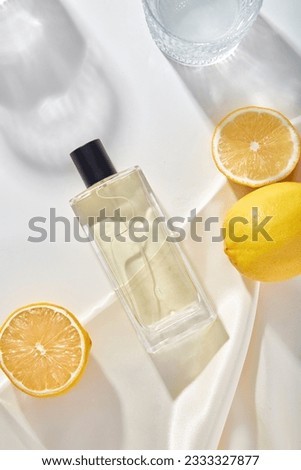 Concept for a perfume advertisement with the scent of fresh lemons. A glass bottle of unlabeled perfume decorated on a white background with fresh lemons, white silk fabric and shadows of glass cup Royalty-Free Stock Photo #2333327877