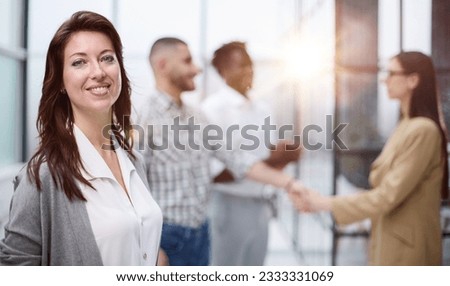 ambitious business woman smiling at the camera against the backdrop of a meeting of colleagues