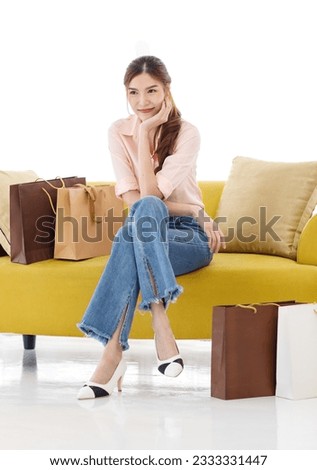 Portrait isolated cutout studio shot of Asian cheerful female client customer shopper in casual outfit sitting on cozy sofa take break buying stuff in paper shopping bags in store on white background. Royalty-Free Stock Photo #2333331447