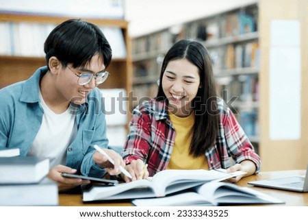 Young students campus helps friend catching up and learning. University students in cooperation with their assignment at library. Group of young people sitting at table reading books. 