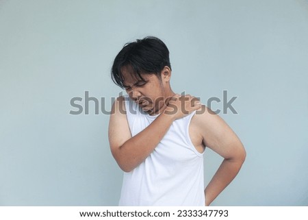 Young asian man wearing casual clothes holding his shoulder with pained and sad expression.
