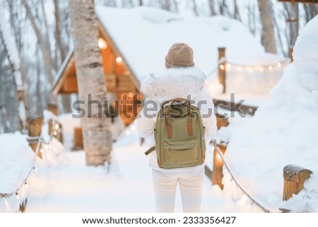 Woman tourist Visiting in Furano, Traveler in Sweater sightseeing Ningle Terrace Cottages with Snow in winter. landmark and popular for attractions in Hokkaido, Japan. Travel and Vacation concept