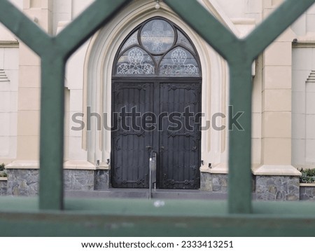 a catholic church door photographed in the gap in the green fence in front of the church