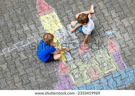 Two little kids boys drawing knight castle with colorful chalks on asphalt. Happy siblings and friends having fun with creating chalk picture and painting. Creative leisure for children in summer. Royalty-Free Stock Photo #2333419969