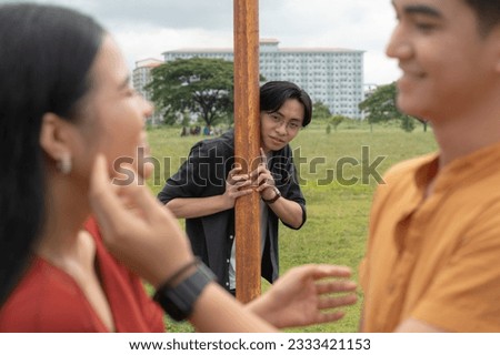 A silly guy conspicuously observes a couple while hiding behind a light pole. Royalty-Free Stock Photo #2333421153
