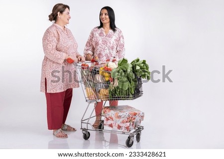 Two woman shopping together, riding shopping trolley isolated over white background,