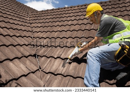 Worker man using silicone sealant adhesive  to fix crack of the old tile roof. Royalty-Free Stock Photo #2333440141