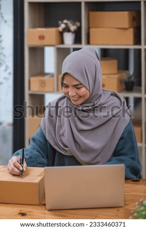Muslim asian woman freelancer working and checklist and writing order with cardboard box at home - SME business online and delivery concept
