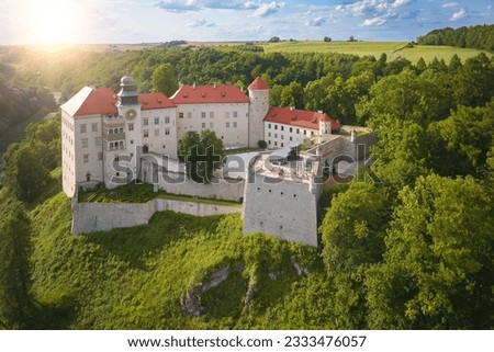 Aerial view of Pieskowa Skała Renaissance castle, standing on Little Dog's Rock  limestone cliff in the forest valley of river Prądnik. Stone Castle among trees, red roofs, sunset,tourist spot,Poland. Royalty-Free Stock Photo #2333476057
