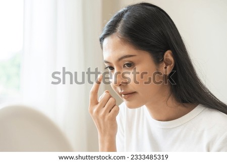 Ophthalmology care, eye sight, vision concept. Asian young woman, female hand holding and putting, wearing soft contact lenses with finger on face, girl looking in mirror at home. Medicine and health. Royalty-Free Stock Photo #2333485319
