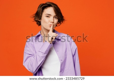 Young caucasian woman she wearing purple shirt white t-shirt casual clothes say hush be quiet with finger on lips shhh gesture isolated on plain orange background studio portrait. Lifestyle concept Royalty-Free Stock Photo #2333485729