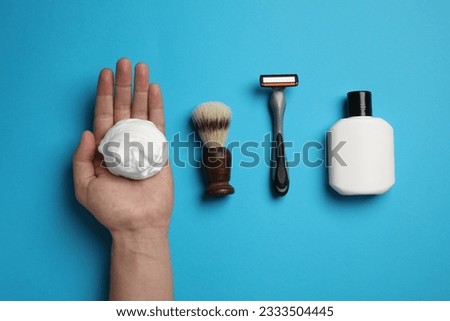 Man with shaving foam, brush, razor and bottle on light blue background, top view Royalty-Free Stock Photo #2333504445