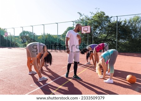 Diverse group of women with male coach stretching and warming up at basketball court. Sport, activity, togetherness and lifestyle, unaltered.