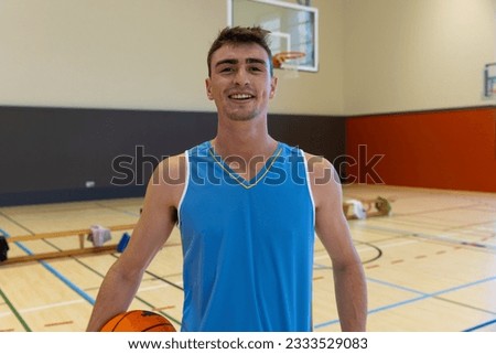 Portrait of happy caucasian male basketball player wearing blue sports clothes at gym. Sport, activity and lifestyle, unaltered.