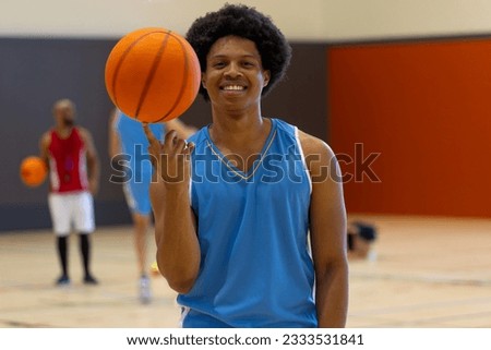 Portrait of happy biracial male basketball player doing trick with basketball over teammates at gym. Sport, activity and lifestyle, unaltered.