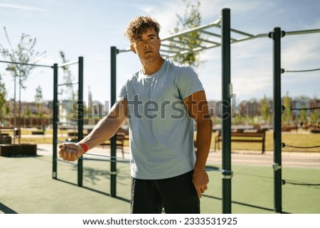 Handsome young man with blond hair dressed in sportswear doing calisthenics at a barbell park with a resistance band on a sunny day