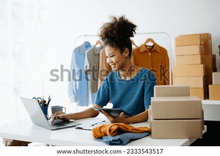 Young African woman running online store Startup small business SME, using smartphone or tablet taking receive and checking online purchase shopping order