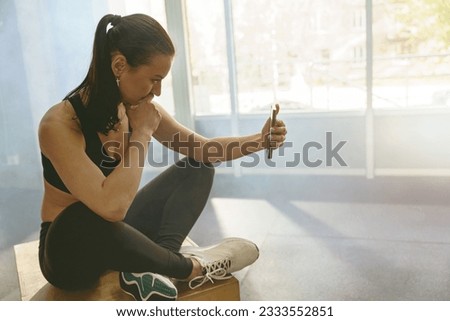 Smiling fit woman in sportswear use phone after workout in gym during resting