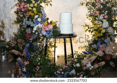 White wedding cake in the evening. Cake on the background of an arch of fresh flowers.	
