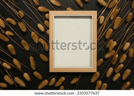 Empty wooden picture frame surrounded by dried fluffy bunny tails grass on black background