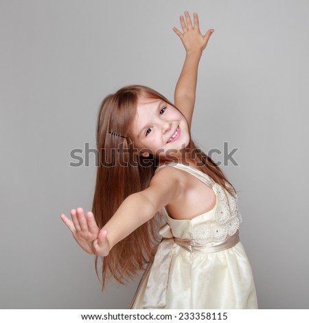 Studio image of a cheerful emotional little girl in a beautiful dress is dancing and having fun on a gray background