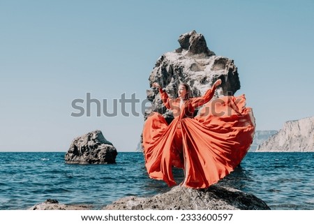 Woman travel sea. Happy tourist in long red dress enjoy taking picture outdoors for memories. Woman traveler posing on beach at sea surrounded by volcanic mountains, sharing travel adventure journey