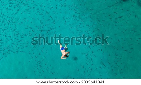 Aerial top view of woman swims with the fishes in the lagoon from above, tropical vacation holiday concept. Mediterranean sea. Aerial seascape with woman, clear blue water, waves in summer. 