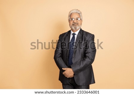 Portrait of senior indian businessman wearing black suit and tie standing isolated over beige background. Copy space. Royalty-Free Stock Photo #2333646001