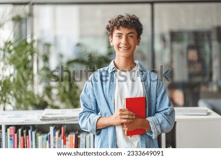 Portrait of smiling smart curly haired teenage boy holding book looking at camera. Back to school, Education concept Royalty-Free Stock Photo #2333649091