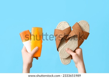 Male hands with flip flops and bottles of sunscreen cream on blue background