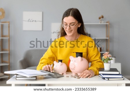 Young female student calculating finances at table with piggy banks. Student loan concept Royalty-Free Stock Photo #2333655389