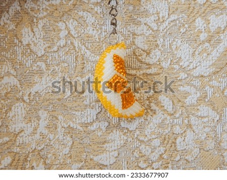 Decorative yellow floral key chain accessory on a chain. Bead colorful key chain on a beige