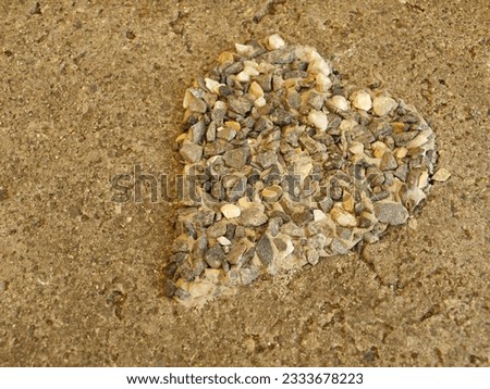 a hand-made heart of gray and brown small stones on a concrete slab
