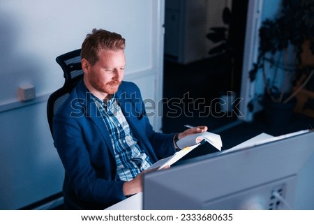 Confident businessman sitting at his desk reading and signing contracts and financial reports while working late in an office
