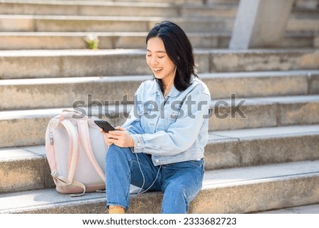 Portrait smiling young woman sitting with phone and bag outside