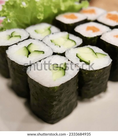 a photography of a plate of sushi with cucumbers and lettuce, there are many sushi rolls on a plate with lettuce.
