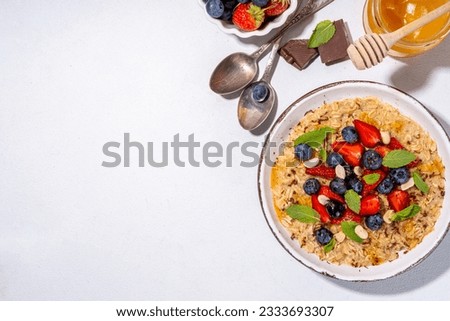Summer breakfast oatmeal with strawberry, blueberry, nuts, chocolate and honey top view copy space, traditional summer fruit and berry oats porridge Royalty-Free Stock Photo #2333693307