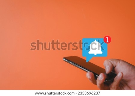 Notification,Alert bell,Alarm bell,reminder,social media concept.,Hand using smartphone with alarm bell ringing icon over orange background with copyspace perfect for technology idea. Royalty-Free Stock Photo #2333696237