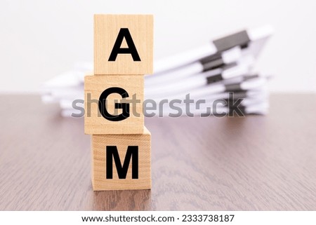 wooden cubes with letters AGM arranged in a vertical pyramid, stack white paper on background