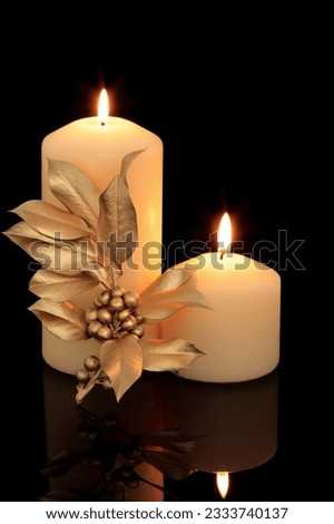 Christmas candle table setting with golden holly berry leaf sprig decoration over black background with reflection.