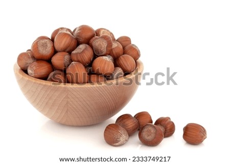 Hazelnuts in a beech wood bowl and loose isolated over white background.
