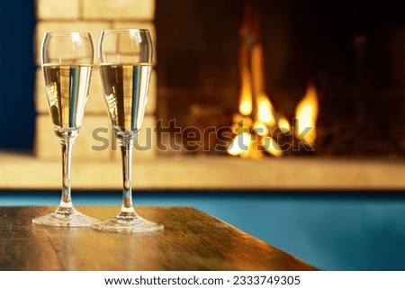 closeup of two wine glasses with champagne on table and fireplace in background. Horizontal shape
