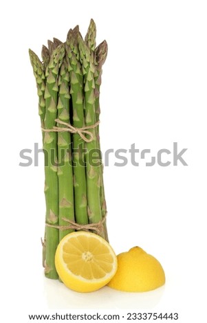 Asparagus spears tied in a bunch with string with two lemon fruit halves isolated over white background.